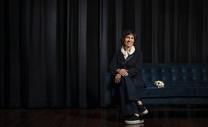 Picture of Deborah Riley sitting right of screen with black curtain behind her 